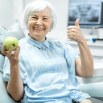 elderly woman holding a green apple and giving a thumbs up 