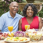 couple sitting outside at a table with various foods and drinks 