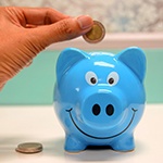 Hand putting coin in blue piggy bank