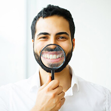 man in white dress shirt holding magnifying glass to his white smile 